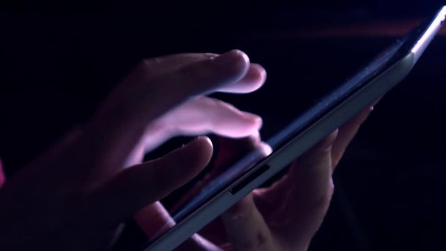Hand gestures over tablet computer in dark room. Purple glowing touchscreen 4K video