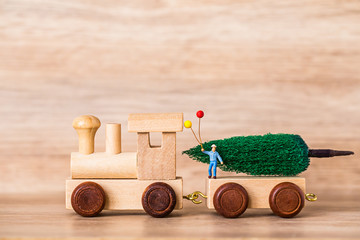 Miniature Figure Toy Wooden Train carry Christmas tree on wooden background, Image for Christmas Holiday decorative concept.