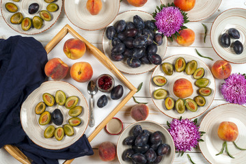 Colorful fruit set of purple, red and orange background in bowls. Plum, peaches, watermelon sliced above white tabletop