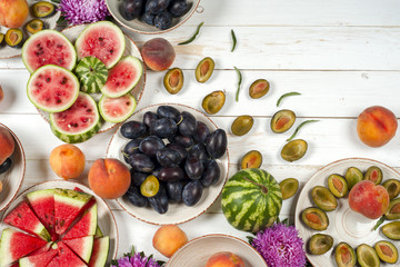 Colorful fruit set of purple, red and orange background in bowls. Plum, peaches, watermelon sliced above white tabletop