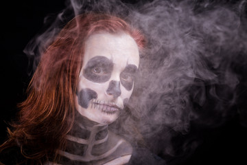 une femme rousse maquillée en squelette sur fond noir avec de la fumée