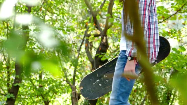 Teenager boy with skateboard walking in the park