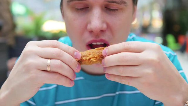 guy eats fried chicken in a fast food restaurant closeup