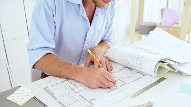 Successful architector correcting drawings sitting at workplace Slow motion