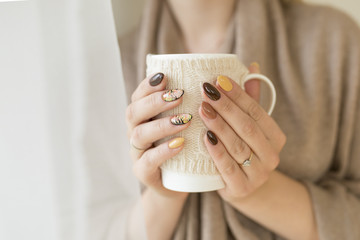 hands of autumn nails holding a cup of hot tea