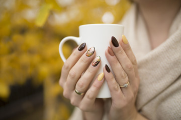 hands of autumn nails holding a cup of hot tea