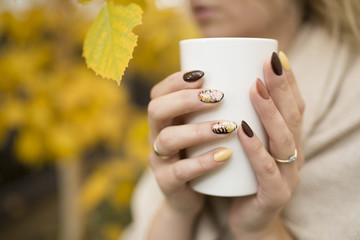 hands of autumn nails holding a cup of hot tea