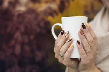 hands of autumn nails holding a cup of hot tea