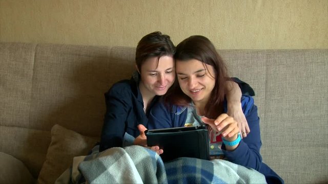 Lesbian girls couple kissing and using a tablet on the sofa at home