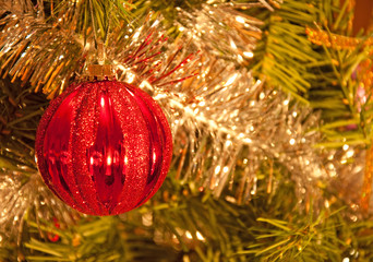 Beautiful red Christmas baubel hanging in a tree adorned by shiny silver tinsel and its reflections