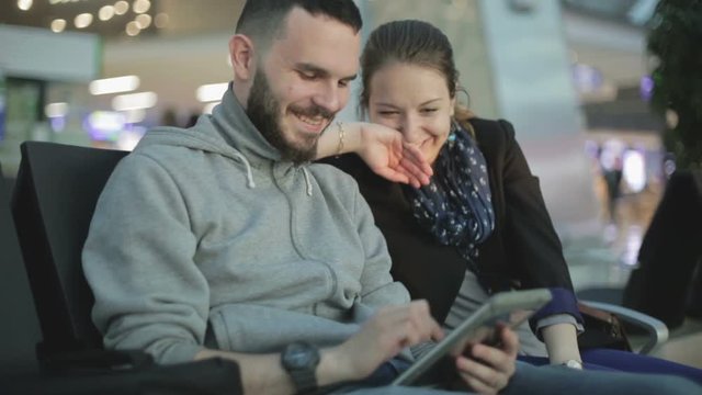 A young girl and her boyfriend are playing a game on the tablet and laugh.