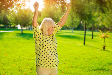 Older woman outdoors. Smiling lady with raised arms. The lucky winner. Enjoy the triumph.