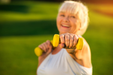 Senior woman holding dumbbell. Elderly lady with smiling face. I train to become healthier. Fight with the laziness.