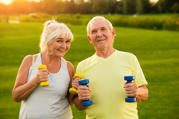 Couple with dumbbells is smiling. Old man and woman outdoors. All goals are achievable. Stay...
