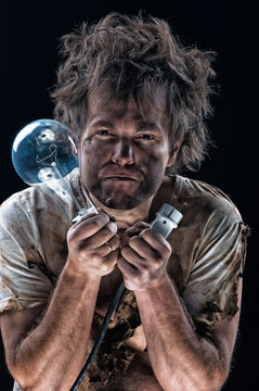 Portrait of burnt man with light bulb and electric plug over black background. Young man with dirty burnt face in funny sad expression in electricity DIY has a electric shock.