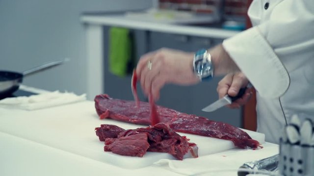 Chef cut up beef tenderloin. Male chef cuts thin slices of meat from a piece of beef. Cooking restaurant meal. Cooking TV. Video recipes. Meat dish. Choice beef on a cutting board.