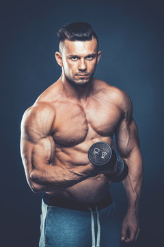 Closeup of a muscular young man lifting dumbbells weights on dar