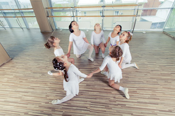 group of seven little ballerinas sitting on the floor. They are 