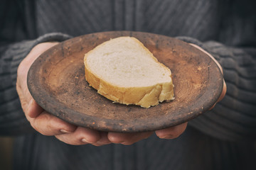 Old man's hands holding rustic plate with one slice of bread. Concept image for poverty.