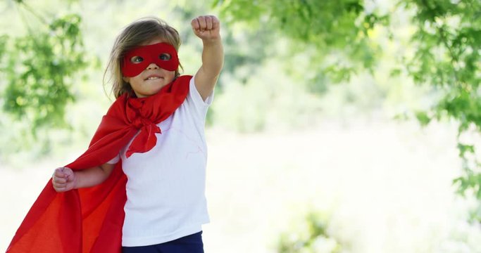 in a beautiful and happy sunny day , a little girl dressed as a super hero makes expressions and try to fly in the colorful nature , the child laughs happy . concept of happiness , love and nature.