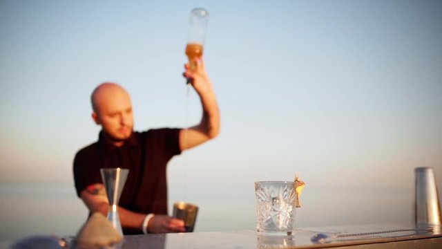 Young handsome bartender preparing cocktail in shaker at seaside Slow motion