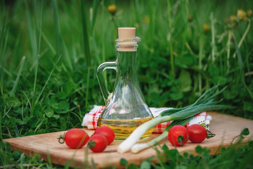On a green meadow food on a wooden Board. On the Board are red tomatoes, green onions and olive oil in the bottle. Healthy food outdoors.