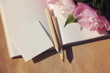 Bouquet of pink peonies on an open notebook and two wooden pencils