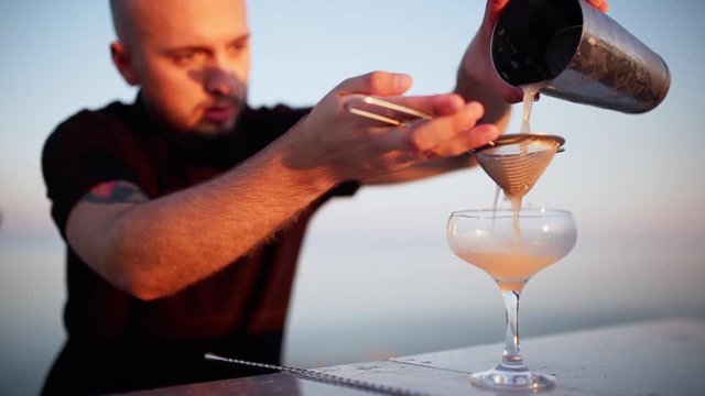 Young professional bartender preparing cocktail outside Sea background Slomo