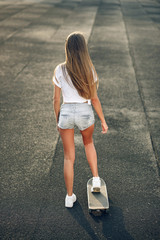 Cute beautiful young and sexy girl in a white T-shirt, shorts and sneakers ride a skateboard