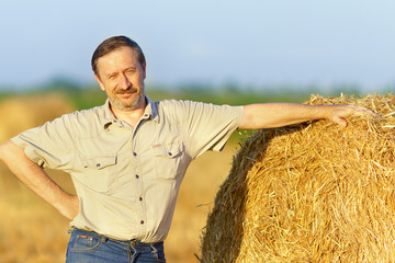 Naklejka na ściany i meble An elderly man is standing next to a stack of straw