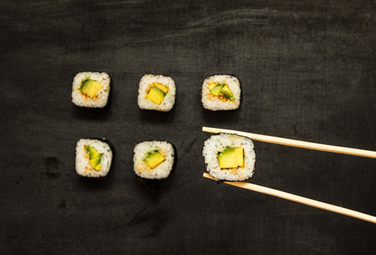 Sushi rolls with avocado maki taken wooden chopsticks. Vegetarian food