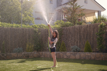 Fototapeta na wymiar Girl playing in the garden getting wet with the hose