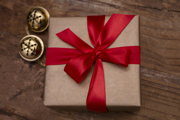 Christmas present on wooden background with gold bells and red ribbon, gold wrapping paper