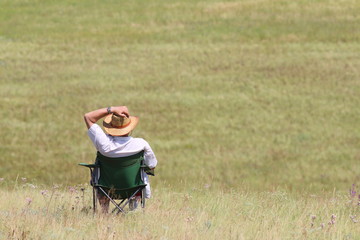 Middle-aged man in a cowboy hat and white shirt sitting in a folding chair, enjoying the steppe freedom