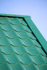 Green modern roof covered with tile effect PVC coated metal roof sheets against a blue sky