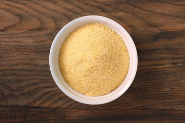 Corn flour polenta in white bowl on dark brown wooden background