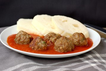 Czech meal from meatballs, tomato sauce and dumpling on white plate on grey cloth with black background