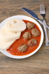 Czech meal from meatballs, tomato sauce and dumpling on white plate on grey cloth