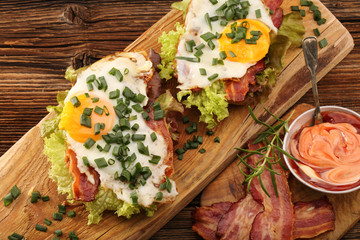 Sandwich with fried bacon, egg and vegetables on wooden backgrou