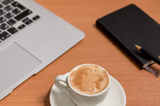 The cup of coffee on the flat workspace with paper notebook, pen and notebook's keyboard on the background. Relax during business day concept.