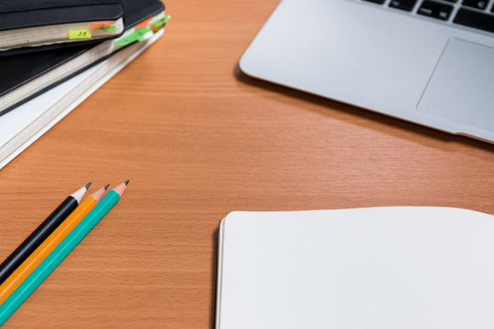 Working space with closed old notebooks with colored bookmarks and one open notebook. Three  ready to use pencils and notebook's keyboard on the background.
