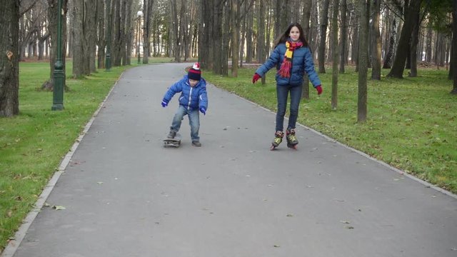 Boy and girl ride in autumn park on rollerblades and scateboard