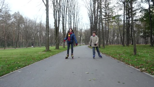 Boy and girl ride in autumn park on rollerblades