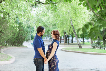 Fototapeta premium Happy pregnant woman with husband standing together in foliage.