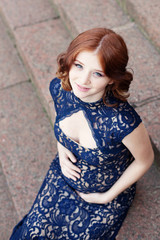 Fototapeta premium Beautiful young red hair pregnant woman sitting on stairs 