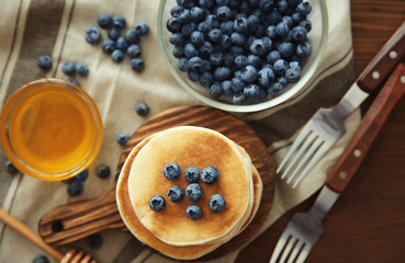 Stack of delicious pancakes with blueberries on wooden cutting board