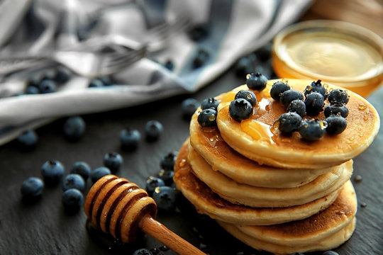 Stack of delicious pancakes with blueberries and honey on slate