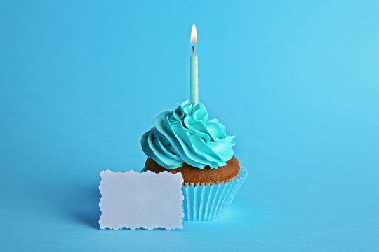 Fresh tasty cupcake with candle and birthday card on blue background