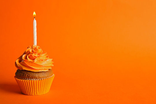 Fresh tasty cupcake with candle on orange background