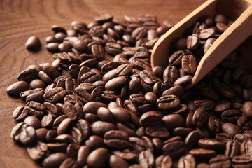 Coffee beans and scoop on wooden background, close up view